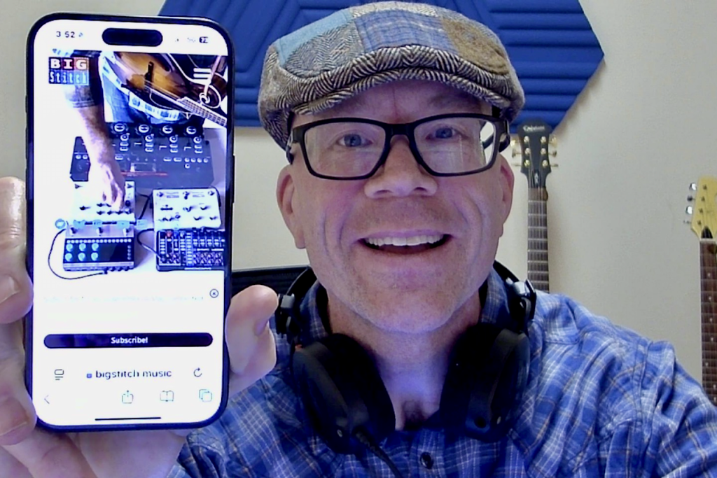Scott Miles holding up his phone showing the website of his new music project, Big Stitch